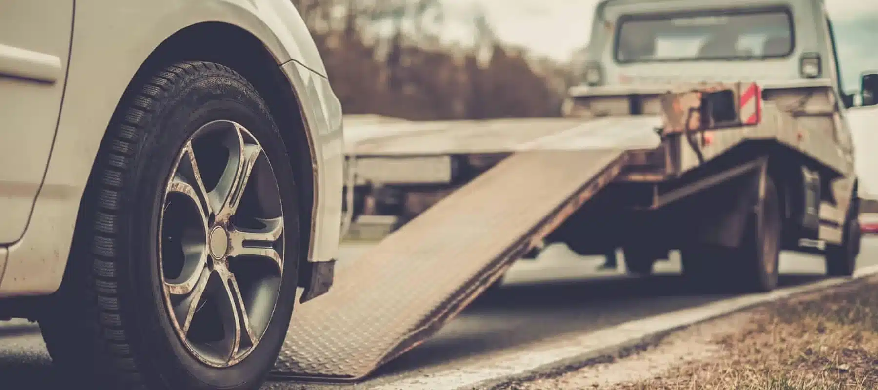 Close-up of a car wheel approaching a tow truck ramp, ready for towing on a roadside.