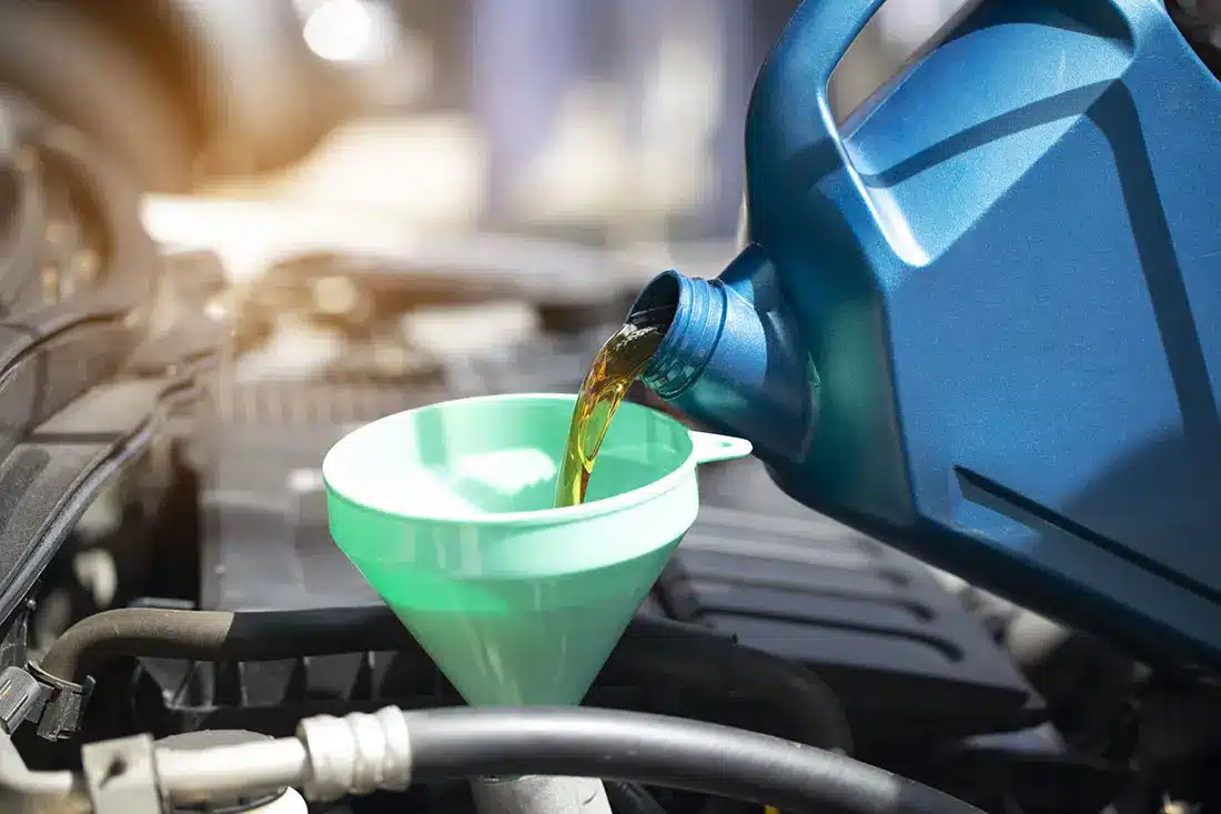 Pouring engine oil from a blue container into a green funnel under a car hood.