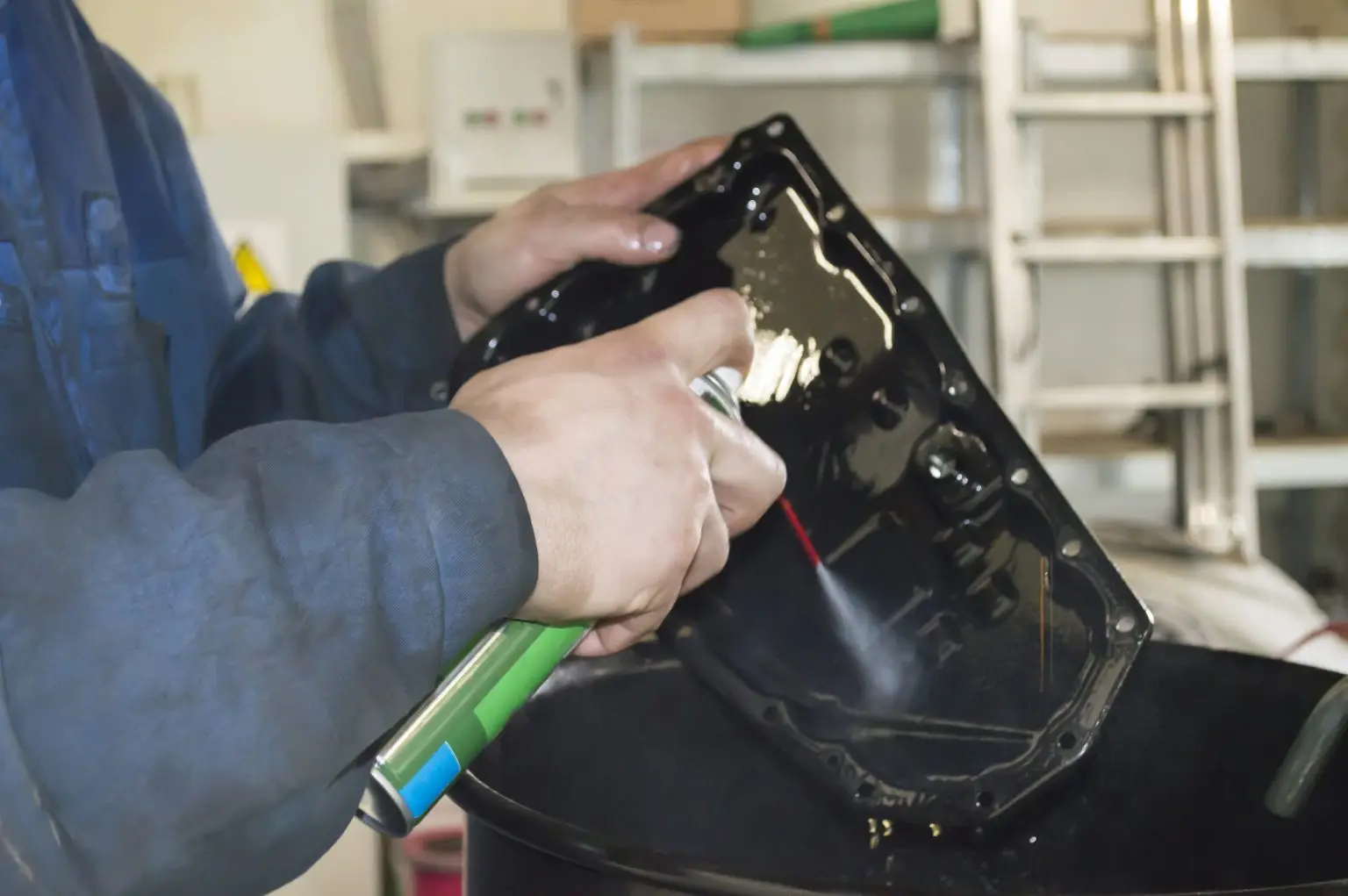 Mechanic cleaning engine part with spray in workshop setting.