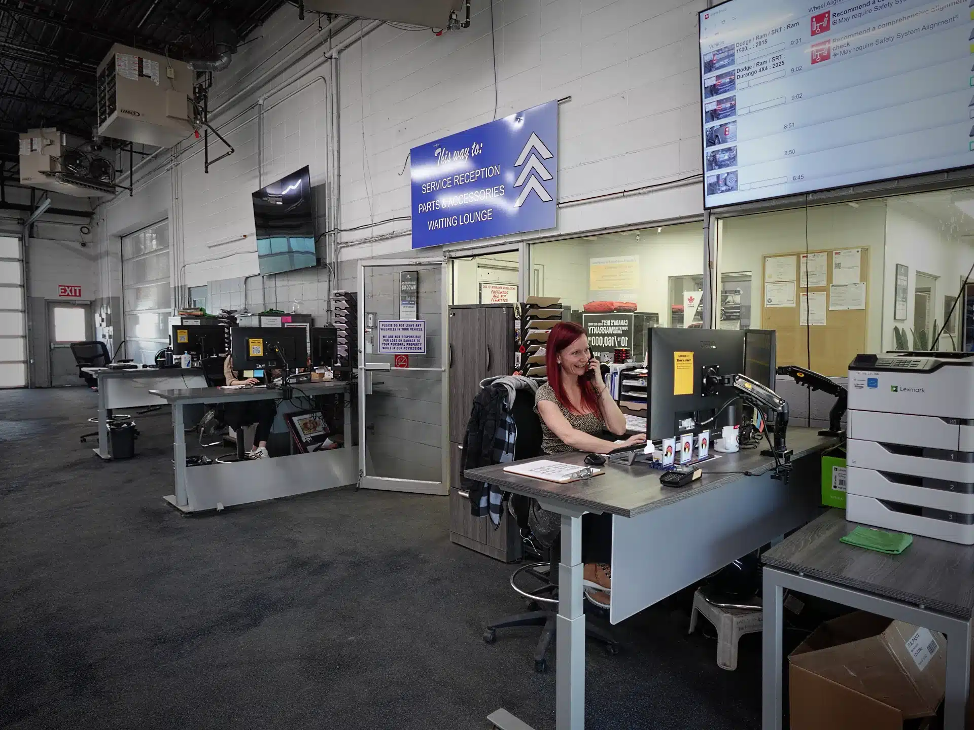 Auto service reception with staff working at desks, computers, and wall signage.